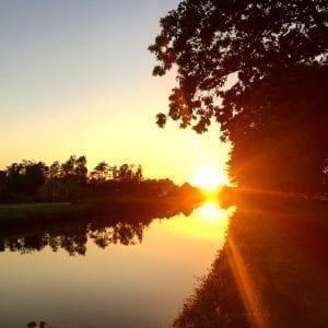 The sun is setting over a canal with golden trees in the background.