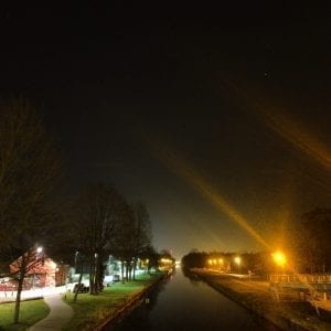 A nighttime canal illuminated by an advertising light.