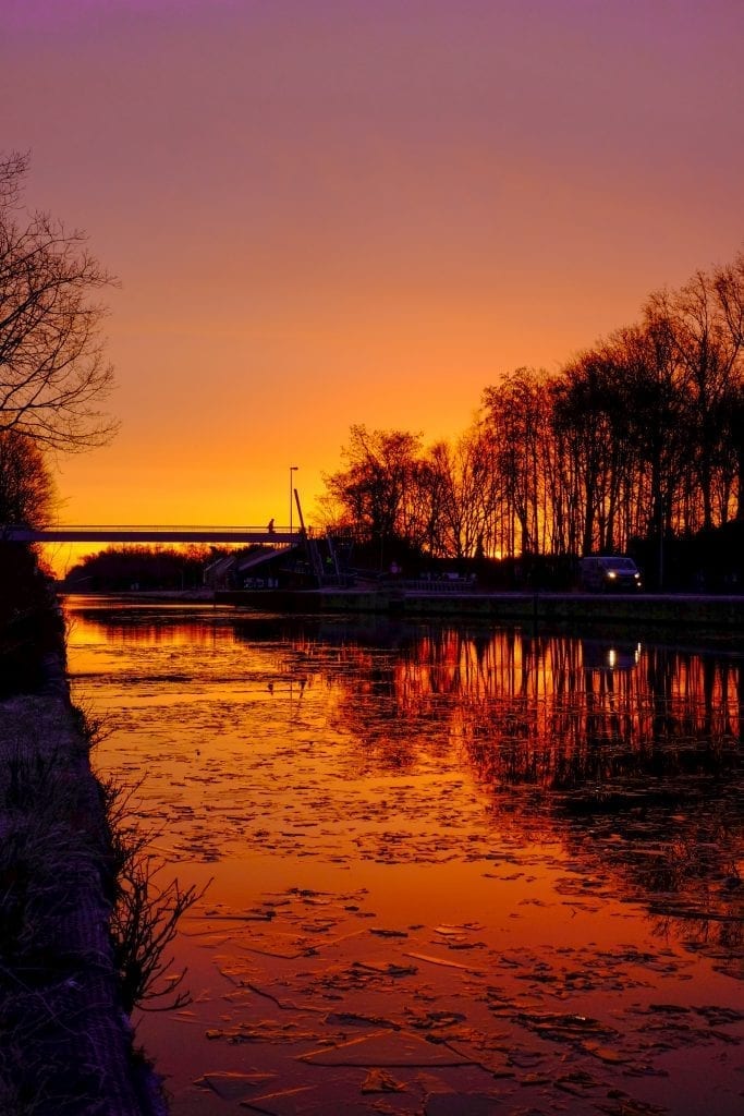 Dramatic and colorful sunrise over a Beautiful early winter landscape with a frozen river or canal, treelined riverside and grass at sunrise creating a tranquile and quiet scenic nature background