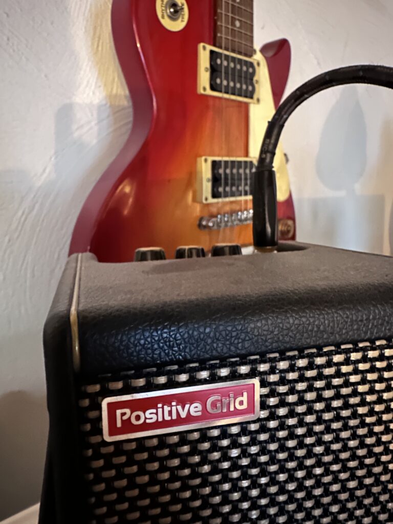 A positive guid amp sitting on a table next to a guitar in the Positive Grid Spark Series.