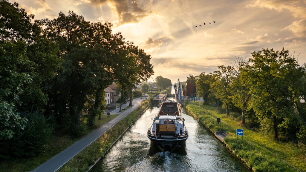 A boat gracefully gliding down a canal at sunset, captured by the powerful DJI Air 3 drone for an impeccable aerial view.
