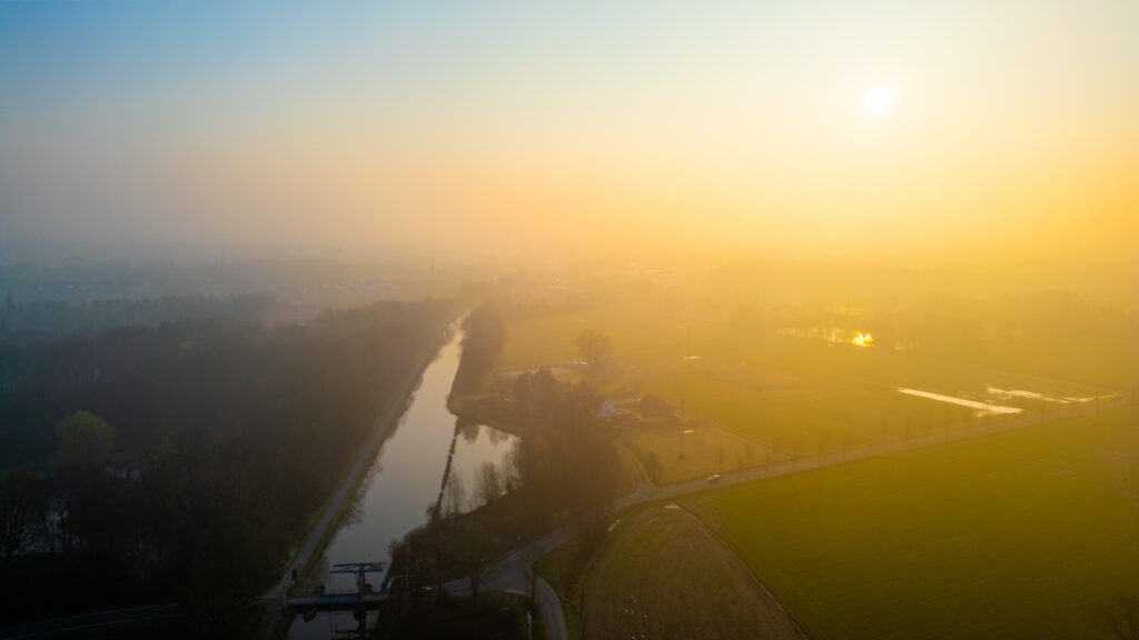 Aerial view of a river winding through a misty landscape at sunrise.