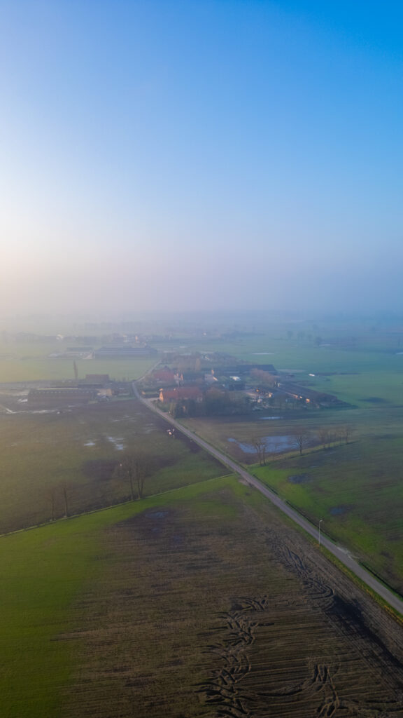 Aerial view of a rural landscape shrouded in light fog with a road leading towards a small village at dawn.
