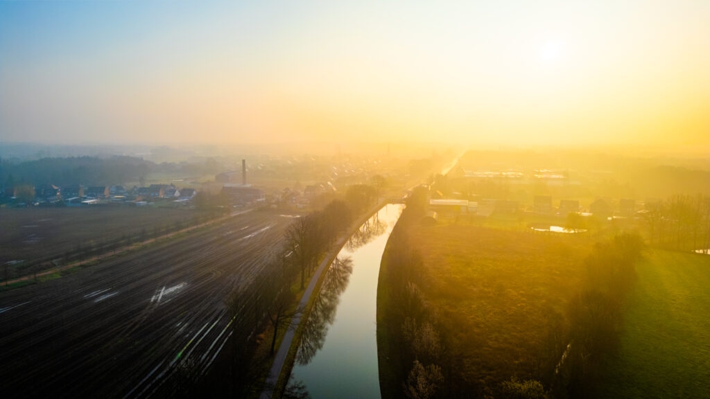 Aerial view of a river winding through a rural landscape at sunrise with haze in the atmosphere.