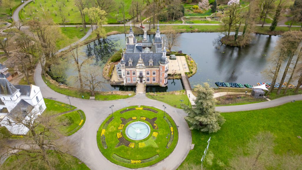 Drone's view of the Castle of Huizingen estate surrounded by a pond and landscaped gardens.