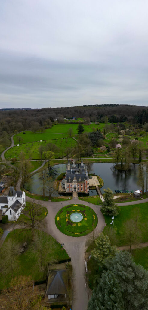 Drone's view of the grand Castle of Huizingen, surrounded by lush gardens, a pond, and winding pathways.