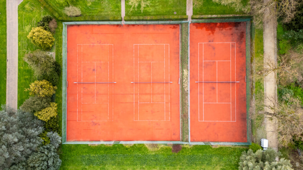 Aerial view of three red tennis courts surrounded by greenery in the Castle of Huizingen.
